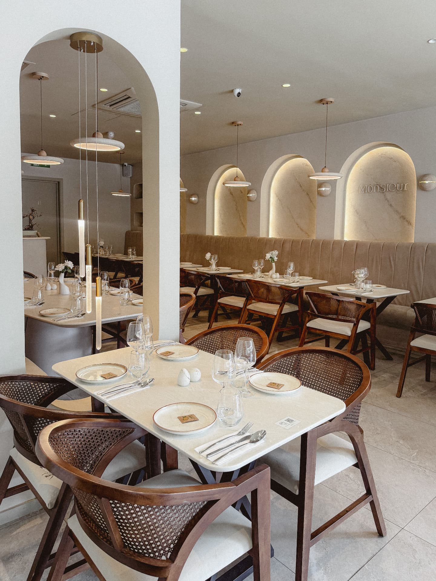 Main dining room at Monsieur with backlit plaster arches, the Monsieur sign, pendant lights and laid marble tables