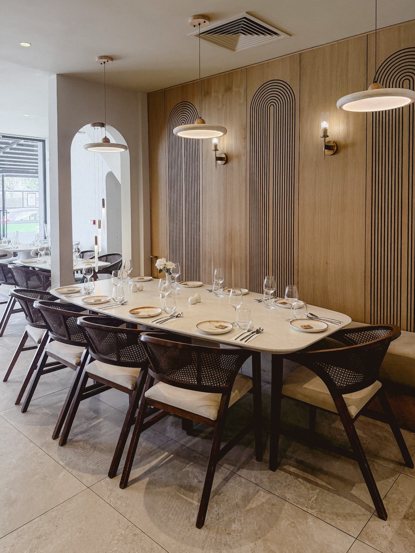 Long celebration table set for a group beneath modern disc pendants, against the oak arch-panelled wall